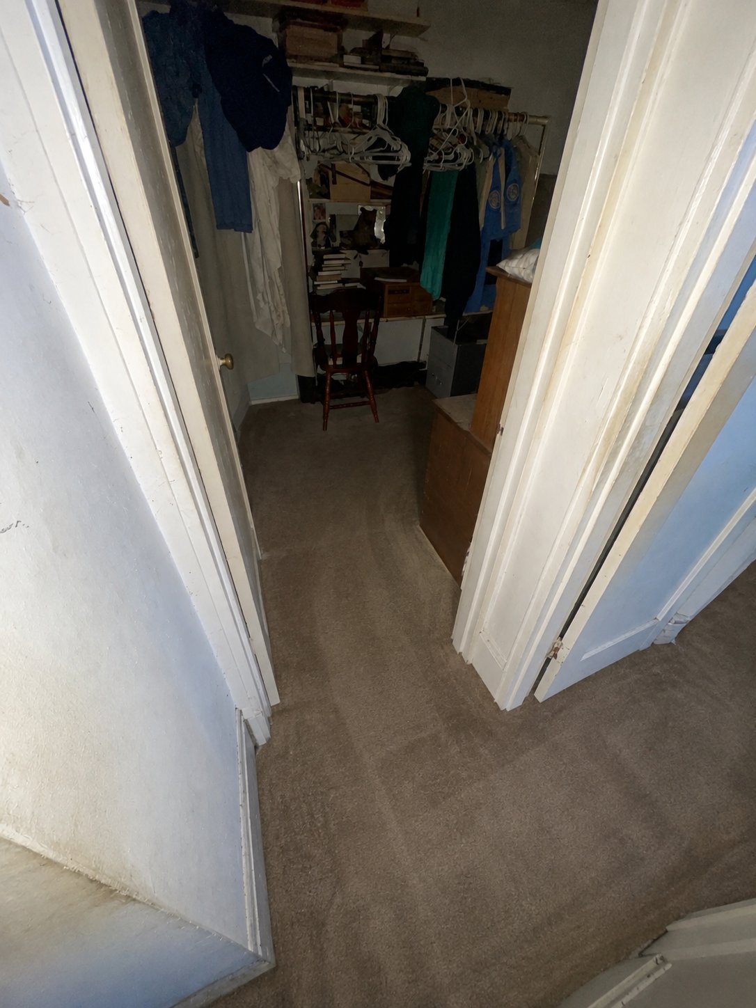 Open closet doors revealing interior with clothes hanging on rack, wooden chair, and carpeted floor