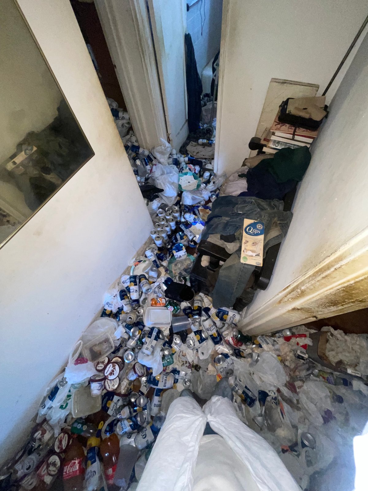 Cluttered hallway or corridor filled with scattered trash, debris, and discarded items piled on the floor between white walls